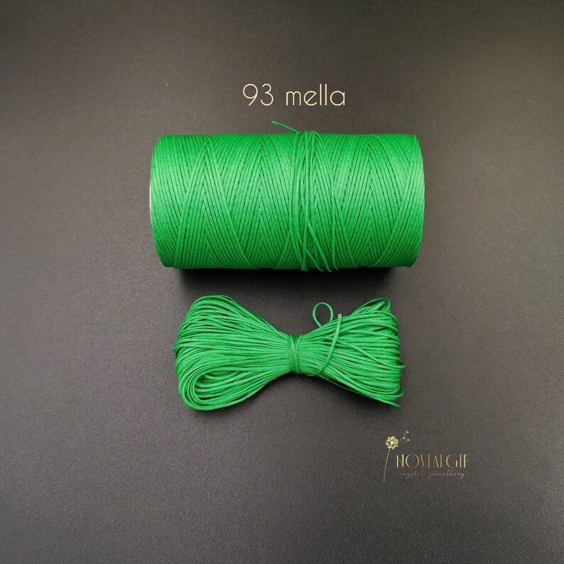 May include: A spool of bright green waxed cord, with a small bow of the same cord, on a black background. The text "93 mella" is printed above the spool.