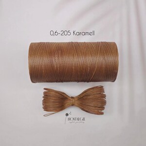 Könnte beinhalten: Eine Spule aus karamellfarbenem Wachsfaden und ein gebündeltes Bündel desselben Fadens werden gezeigt. Der Text "0,6-205 Karamell" befindet sich über der Spule. Das Logo "NOSTALGIE crystal jewellery" befindet sich unten rechts.