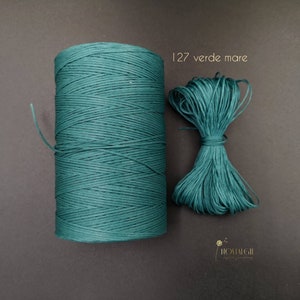 Puede incluir: Una bobina de cordón encerado verde azulado, con un trozo más pequeño del mismo cordón al lado. El texto "127 verde mare" está impreso sobre un fondo blanco.
