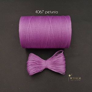 Puede incluir: Una bobina de cordón encerado morado etiquetada "4067 petunia" con un lazo hecho del mismo cordón.