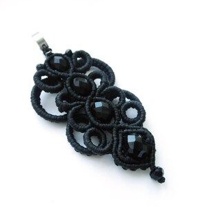May include: Black pendant necklace with a delicate, intricate design made of black cord and black beads. The pendant is shaped like a teardrop and features a repeating pattern of circles and loops.