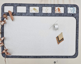 May include: A grey felt beading mat with five compartments for organising beads and tools. The mat has a white surface and is labelled with the letters A, B, C, D, and E. A small beaded earring is on the mat.