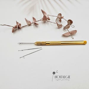 Peut inclure: Un outil doré avec trois embouts en forme d'aiguille. L'outil est utilisé pour enfiler des perles et d'autres petits objets.