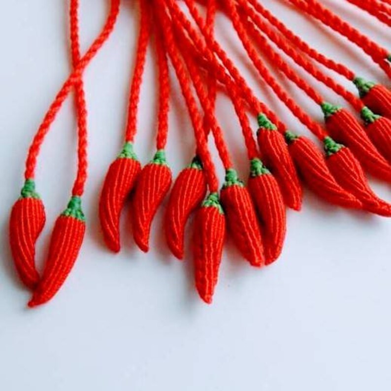 Peut inclure: Un groupe de glands en forme de piment rouge et vert, faits de ficelle, suspendus &agrave; une ficelle.