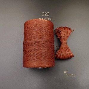 Puede incluir: Una bobina de cordón encerado marrón etiquetada "222 ruggine" con una pequeña muestra del cordón atado en un lazo.