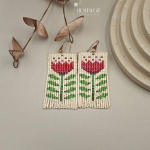 Könnte beinhalten: Ein Paar Perlenohrringe mit einem roten Tulpenmotiv und grünen Blättern. Die Ohrringe sind aus weißen Perlen gefertigt und haben goldfarbene Haken.