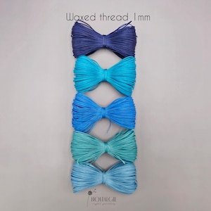 Op de afbeelding: Vijf spoelen gewaxt draad in blauwtinten, van diep marineblauw tot licht aqua. De tekst "Waxed thread 1mm" staat bovenaan. De onderkant van de afbeelding bevat de tekst "nostalgie crystal jewellery".