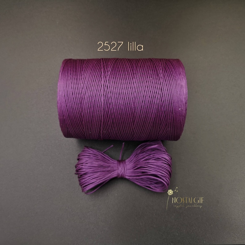 May include: A spool of purple waxed cord, labeled "2527 lilla", with a bow of the same cord in front of it.