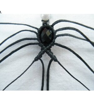 May include: Close-up of a black macrame knot with a black gemstone in the centre. The knot is made with multiple strands of black cord.