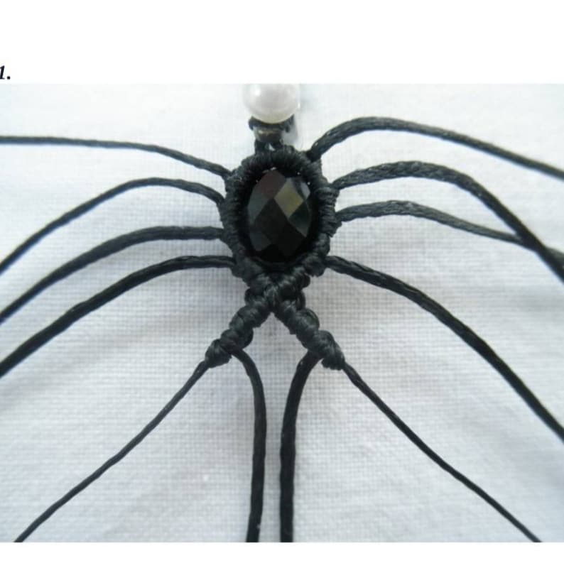 May include: Close-up of a black macrame knot with a black gemstone in the centre. The knot is made with multiple strands of black cord.