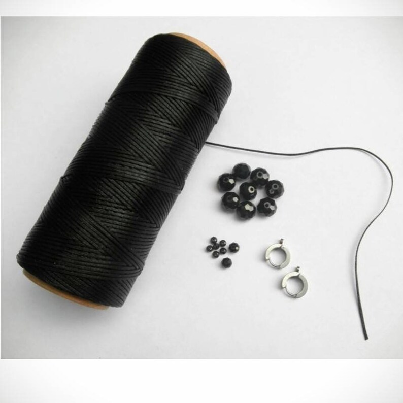 May include: A spool of black waxed cord, a set of black beads, and two silver earring hoops. These supplies are for jewellery making.