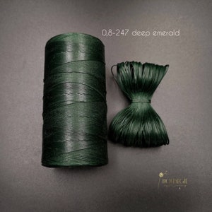 Puede incluir: Una bobina de cordón encerado verde oscuro, etiquetada "0,8-247 deep emerald", con una pequeña muestra del cordón al lado.