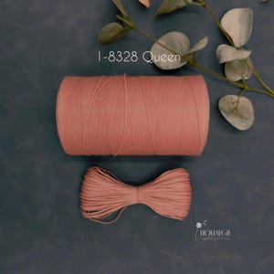 May include: A spool of dusty rose-colored thread and a tied bundle of the same thread are displayed on a dark gray surface. The text "I-8328 Queen" is visible. Eucalyptus leaves are in the background.