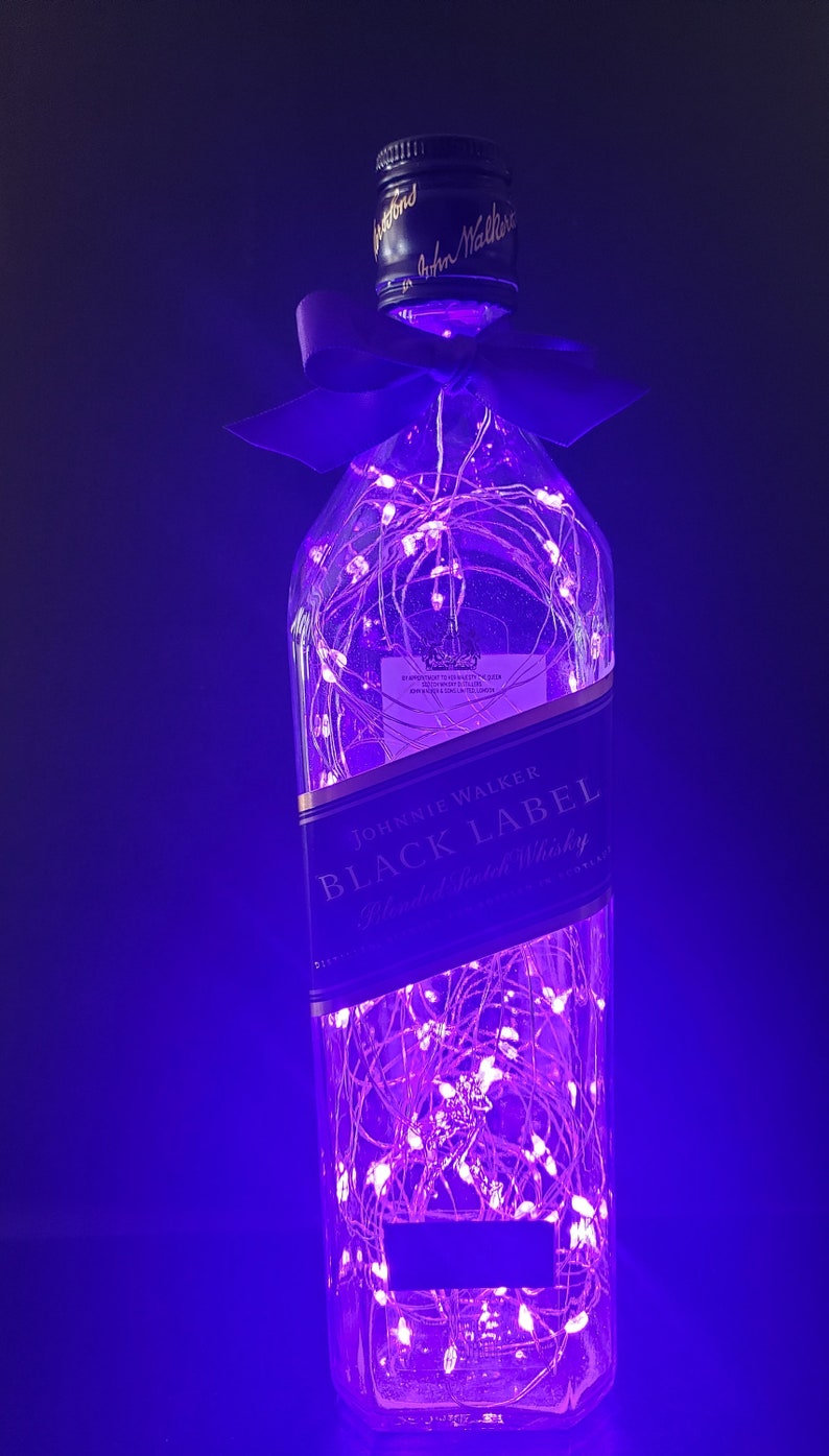 May include: A clear glass bottle with a purple ribbon and string lights inside. The bottle is labeled "Johnnie Walker Black Label Blended Scotch Whisky".