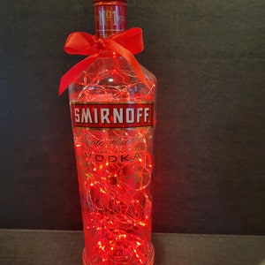 May include: A clear glass bottle with a red ribbon and red fairy lights inside. The bottle is labelled "Smirnoff Triple Distilled" and "Vodka".