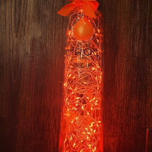 May include: A clear glass bottle of Ciroc Mango vodka wrapped in orange fairy lights with a bow on the top.