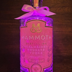 May include: A pink glass bottle with a pink ribbon and fairy lights. The bottle is labelled "Mammoth Distilling Strawberry Rhubarb Vodka".