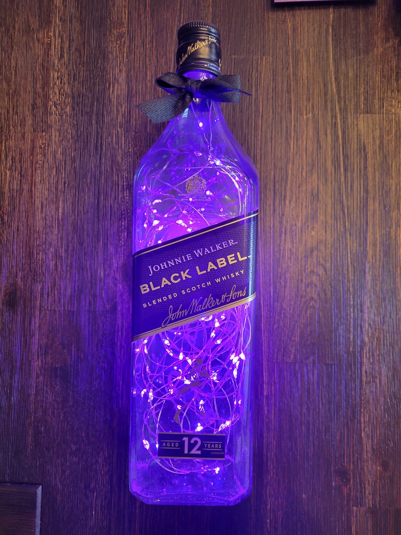 May include: A clear glass bottle with a purple glow from fairy lights inside. The bottle is shaped like a Johnnie Walker Black Label whiskey bottle and has the label text "JOHNNIE WALKER BLACK LABEL BLENDED SCOTCH WHISKY John Walker & Sons AGED 12 YEARS".