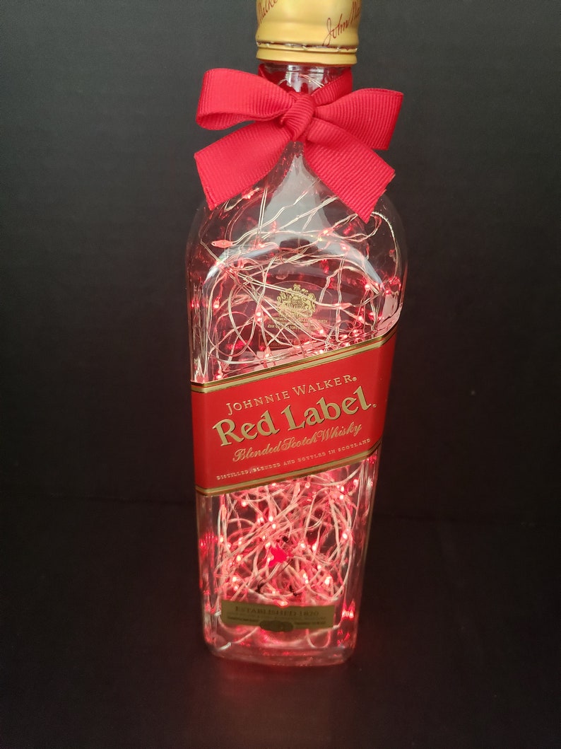 May include: A clear glass bottle with a red bow and red string lights inside. The bottle is labeled "Johnnie Walker Red Label Blended Scotch Whisky".