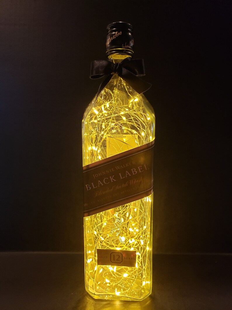 May include: A clear glass bottle with a black bow and string lights inside. The bottle is labeled "JOHNNIE WALKER BLACK LABEL Blended Scotch Whisky 12 YEARS OLD"