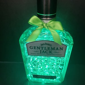May include: A clear glass bottle with a green bow and fairy lights inside. The bottle is labelled "Jack Daniel's Gentleman Jack Double Mellowed - Tennessee Whiskey".