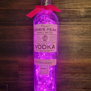 May include: A clear glass bottle with pink fairy lights inside. The bottle is labelled "Original Grays Peak Small Batch" and "Distilled 5 Times Vodka". The label also says "Crafted by Grays Peak Spirits" and "Blend: No. 45".