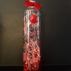 May include: A clear glass bottle with a red ribbon and red lights inside. The bottle is labelled "CIROC Red Berry"