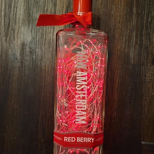 May include: A clear glass bottle with a red ribbon and red lights inside. The bottle is labelled "New Amsterdam Red Berry".
