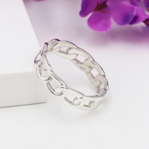 Könnte beinhalten: Ein silberner Ring mit einem Kettenglied-Design. Der Ring besteht aus glänzendem Metall und weist eine Reihe von miteinander verbundenen Gliedern auf. Der Ring ist mit der Nummer "925" gekennzeichnet. Der Ring befindet sich auf einer weißen Oberfläche.