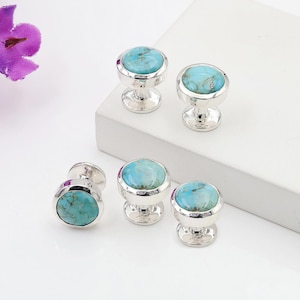 May include: Five silver cabinet knobs with round, light blue turquoise stones. The knobs have a pedestal base and a polished finish. The turquoise stones have natural veining and are set in a silver bezel.