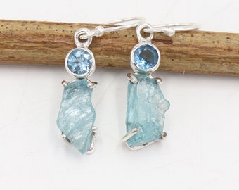May include: Silver earrings with a light blue gemstone and a rough, light blue aquamarine stone.