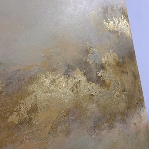 Op de afbeelding: Abstract schilderij met een textuur, gelaagde look. De achtergrond is lichtgrijs met hints van roze en groen. De voorgrond is goudkleurig met een metallic glans.