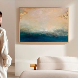 Op de afbeelding: Abstract schilderij met een blauwe en groene oceaan sc&egrave;ne met gouden accenten. Het schilderij is ingelijst in een licht houten lijst.