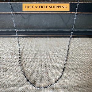 May include: A black chain necklace on a textured fabric background.  The chain is made of small, linked circles.