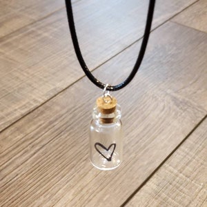 May include: A black cord necklace with a small glass bottle pendant. The bottle has a cork stopper and a hand-drawn heart inside.