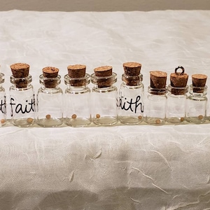 May include: A collection of small glass bottles with cork stoppers. The word "faith" is written on some of the bottles. Each bottle contains a mustard seed. Some bottles have a small gold loop attached to the cork.
