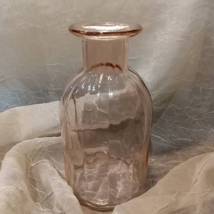 Puede incluir: Un jarrón de vidrio transparente con una superficie texturizada. El jarrón es de color rosa claro y tiene una boca ancha.