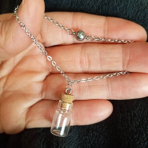 May include: A silver chain necklace with a small glass bottle pendant and a silver bead. The bottle has a cork stopper.