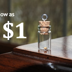 May include: A small glass bottle with a cork stopper and a silver loop on top. The bottle contains a single, small, yellow seed. The text "as low as $1" is visible in the image.