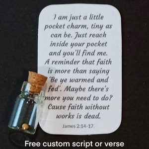 May include: A small glass bottle with a cork stopper containing a single white bead. A white card with the text "I am just a little pocket charm, tiny as can be. Just reach inside your pocket and you'll find me. A reminder that faith is more than saying 'Be ye warmed and fed'. Maybe there's more you need to do? Cause faith without works is dead. James 2:14-17." and the text "Free custom script or verse" is below the bottle.