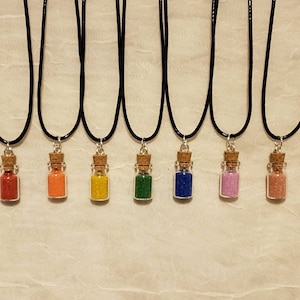 May include: Seven necklaces with small glass bottles filled with colored sand. The bottles have cork stoppers and are attached to black cords.