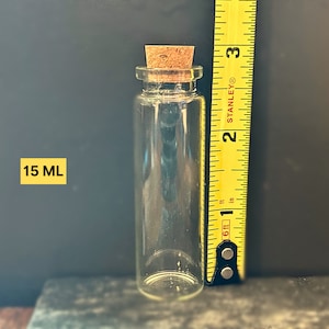 May include: A clear glass bottle with a cork stopper. The bottle is 15 ml and is next to a measuring tape.