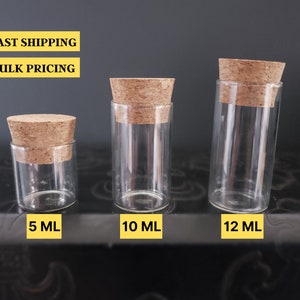 May include: Three glass bottles with cork stoppers, from left to right: 5 ml, 10 ml, and 12 ml. The bottles are clear and the stoppers are brown.