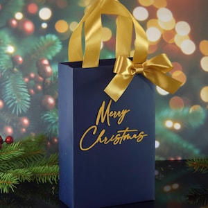 May include: A navy blue gift bag with a gold ribbon and bow. The bag has the words "Merry Christmas" written in gold on the front.