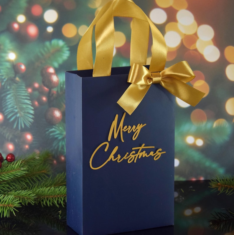 May include: A navy blue gift bag with a gold ribbon and bow. The bag has the words "Merry Christmas" written in gold on the front.