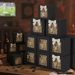 May include: A stack of black gift boxes with white bows, each featuring a window revealing a glass container filled with shredded paper. The boxes are arranged on a wooden table, suggesting a gift or party theme.