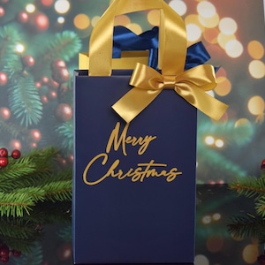 May include: A navy blue gift bag with gold handles and a gold bow. The bag has the words "Merry Christmas" written in gold lettering.