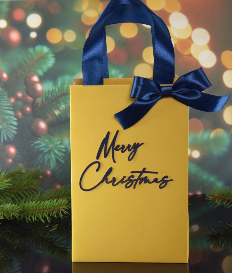 May include: A yellow gift bag with a blue ribbon and the words "Merry Christmas" printed on the front.