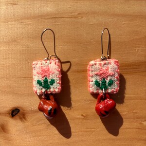 May include: A pair of pink and white floral fabric earrings with red clay bell charms.