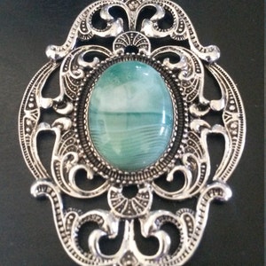 Könnte beinhalten: Ein silberner Filigrananhänger mit einem grünen und weißen Achat-Stein in der Mitte.